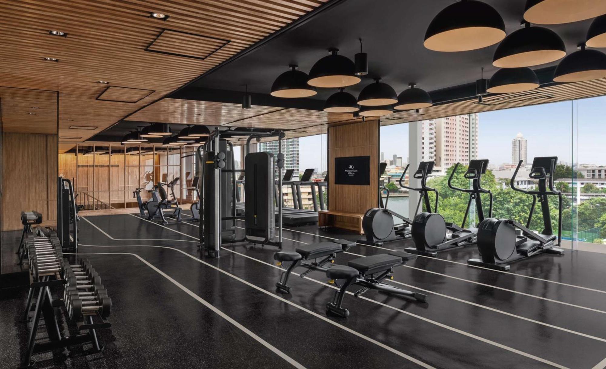 Hotel Millennium Hilton Bangkok Esterno foto The photo depicts a modern gym or fitness center. It features a sleek design with wooden ceiling elements and large windows that allow natural light to flood the space. Various gym equipment is visible, including treadmills, elliptical machines, and 